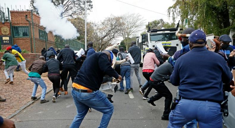 Protesters run from a stun grenade fired by police outside the Zimbabwean Embassy in South Africa's Pretoria