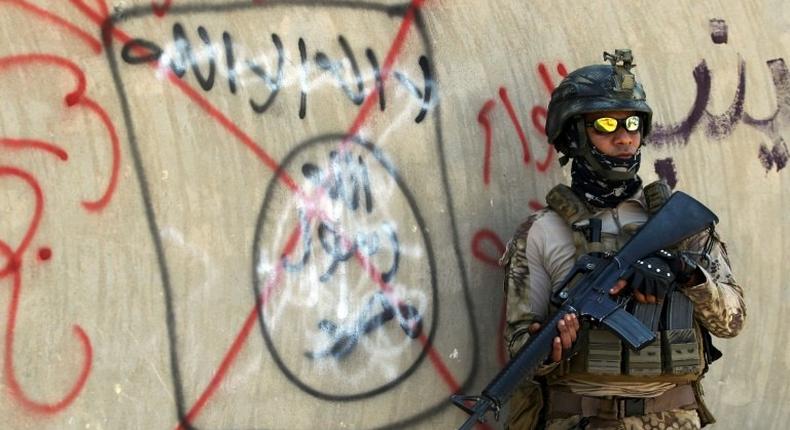 An Iraqi soldier stands next to a wall with a red cross drawn through a slogan of the Islamic State (IS) group, in Fallujah