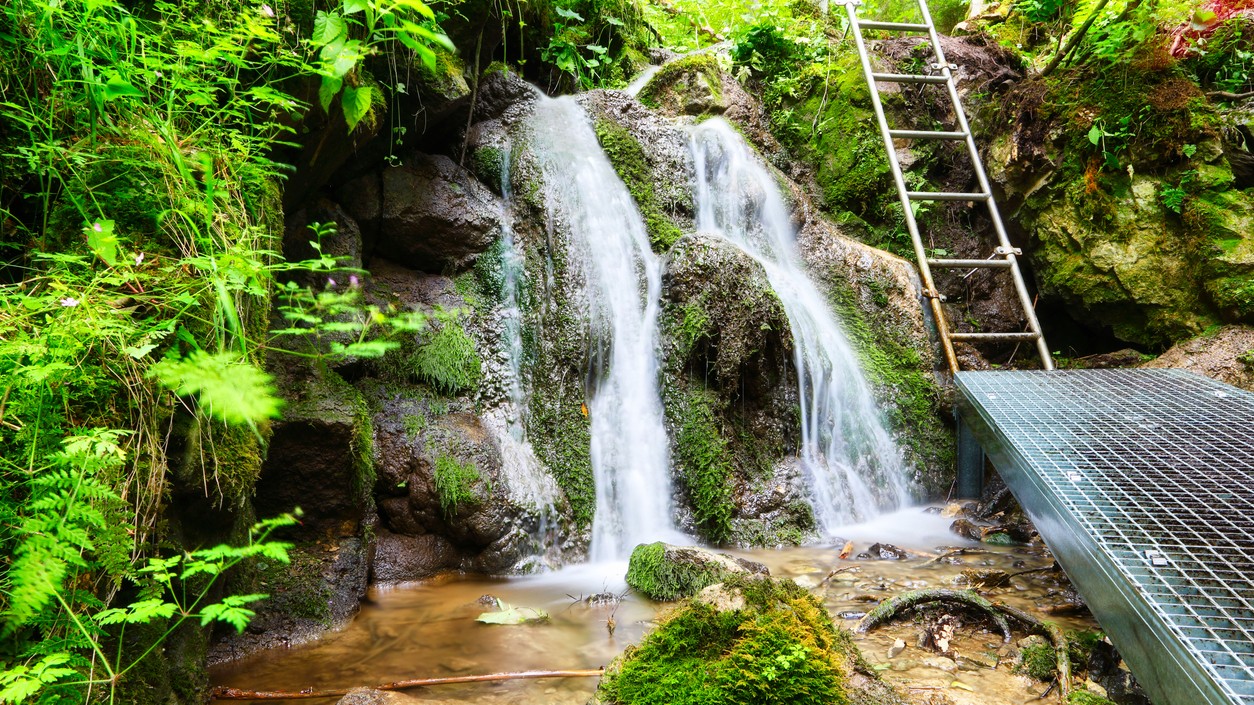 Úchvatný záber vodopádu Hrabovo, ktorý tečie cez skalnaté hory v zelenom lese.