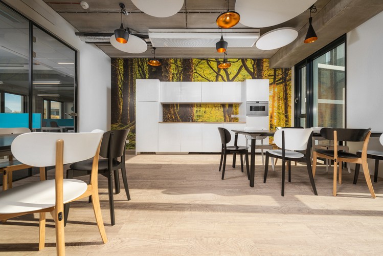 Aranżacja wnętrz pomaga w efektywnej pracy, niezależnie od otoczenia. Równie ważne są przestrzenie do odpoczynku: strefa chillout i kuchnia. Surowy, industrialny wystrój wnętrz, wzmocniony przez betonowe elementy konstrukcyjne oraz odsłonięte sufity, przełamany został pastelowymi kolorami i miękkimi fakturami obić mebli biurowych. Nadają one przestrzeni domowe ciepło.