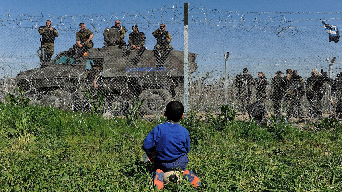 A boy sits on his ball next to a border fence on the Greek side of the border, as Macedonian police 