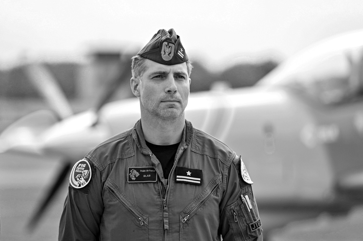Pilot major Maciej "Slab" Krakowian w mundurze na tle samolotu F-16.
