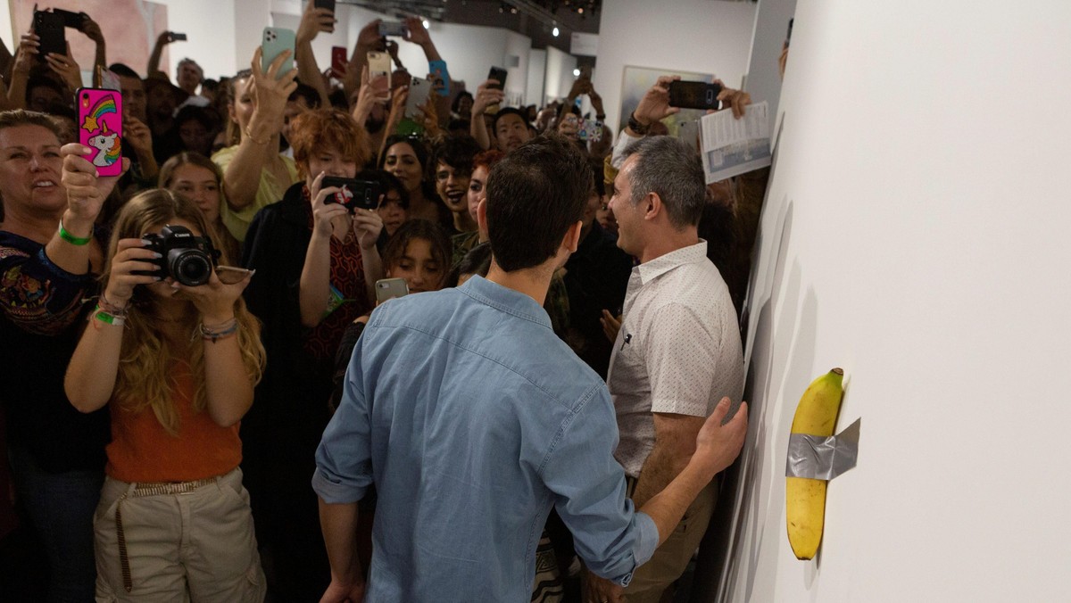 Art Basel visitors use their phones in front of a banana attached with duct-tape that replaces the artwork 'Comedian' by the artist Maurizio Cattelan, which was eaten by David Datuna, in Miami Beach