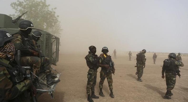 Cameroonian soldiers from the Rapid Intervention Brigade stand guard amidst dust kicked up by a helicopter in Kolofata, Cameroon, March 16, 2016.