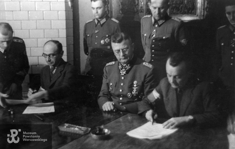Delegaci Komendy Głównej AK podpisują Układ o zaprzestaniu działań wojennych w Warszawie. Od strony lewej siedzą: w okularach płk Kazimierz Iranek-Osmecki „Jarecki” (1897–1984), SS-Obergruppenführer Erich von dem Bach (1899–1972) i ppłk Zygmunt Dobrowolski „Zyndram” (1897–1972)