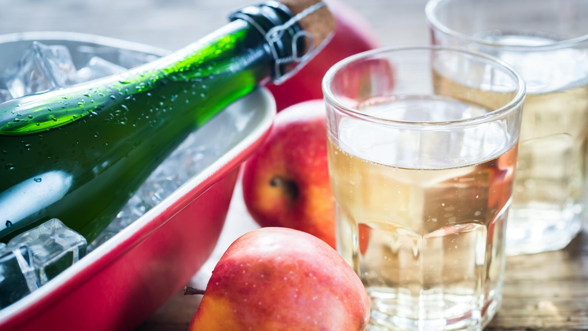 Bottle and two glasses of cider on the wooden background