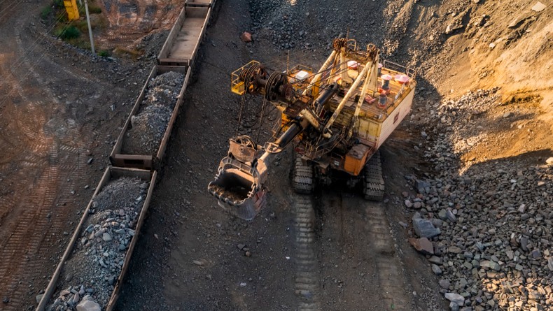 Aerial view of open pit iron ore and heavy mining equipment. Large excavator loads iron ore into train carriages. [Stock Photo via Getty Images]