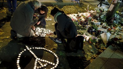 People kneel as they light candles to pay tribute to victims near the site of the attack at the Bata