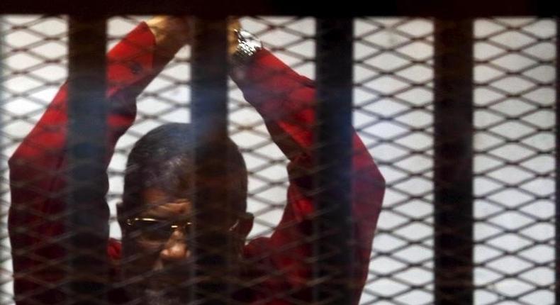 Deposed President Mohamed Mursi greets his lawyers and people from behind bars at a court wearing the red uniform of a prisoner sentenced to death, during his court appearance with Muslim Brotherhood members on the outskirts of Cairo, Egypt, June 21, 2015. REUTERS/Amr Abdallah Dalsh