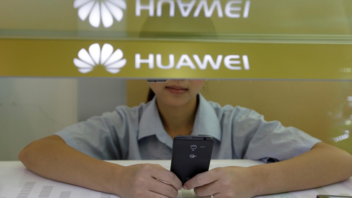 FILE PHOTO: A sales assistant looks at her mobile phone as she waits for customers behind a counter at a Huawei booth in Wuhan