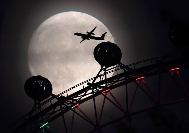 An aeroplane flies past the London Eye wheel, and moon, a day before the supermoon spectacle in Lo