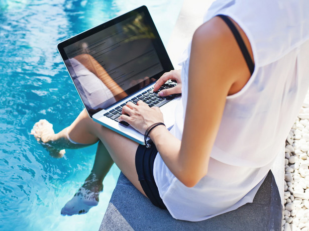 Kobieta z laptopem nad basenem. Praca na urlopie