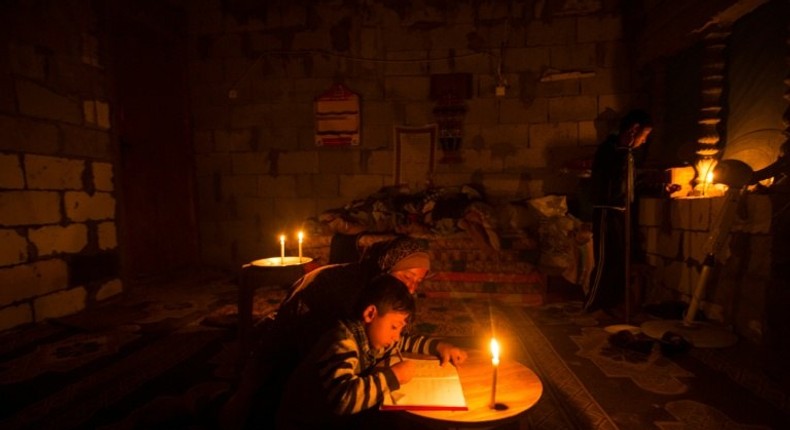 A Palestinian woman helps her son study, by candlelight, at their makeshift home in the Khan Yunis refugee camp in the southern Gaza Strip on April 19, 2017