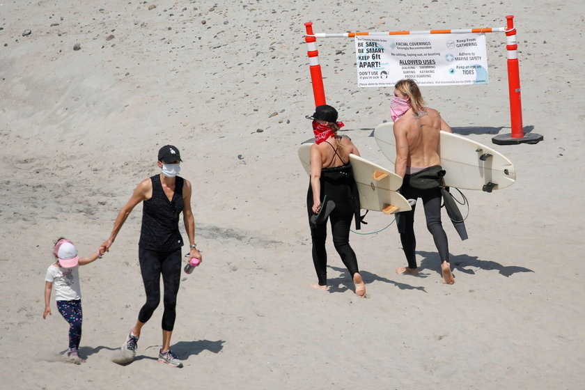 Surferzy przybywają na plażę w maseczkach ochronnych po otwarciu plaż podczas  epidemii koronawirusa