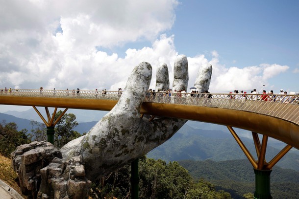 Tourists walk past giant hand structure on Gold Bridge on Ba Na hill near Danang City