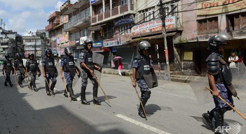 Nepalese police in riot gear walk past shuttered shops in Kathmandu.