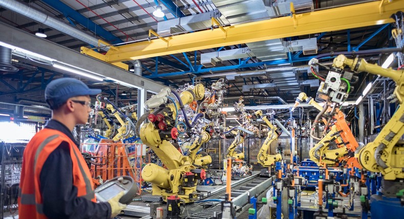 An apprentice engineer programming robots in a car factory