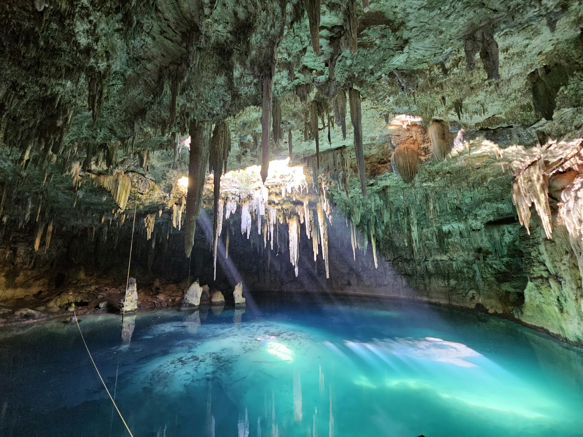 Posvätný krasový kráter Cenote Ik Kil na mexickom poloostrove Yucatán s typickými liánami a smaragdovou vodou.