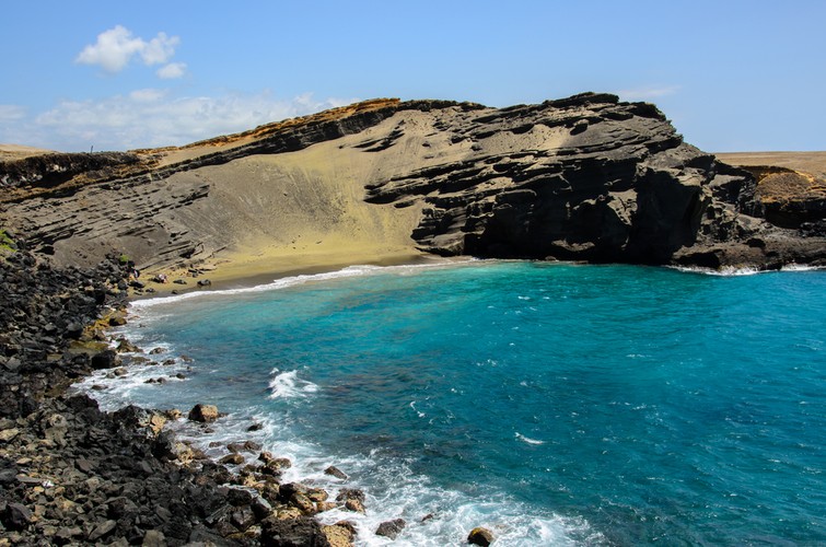 Papakolea - zielona plaża na Hawajach. Ten niezwykły efekt został spowodowany wybuchem wulkanu. To właśnie wtedy kryształy oliwinu osiadły na plaży. Ich ciężar spowodował, że woda nie zdołała zmyć ich do oceanu, jak innych pozostałości po wybuchu. Dzięki temu, turyści na wyspie mają szansę odpoczywać na… zielono-oliwkowej plaży.