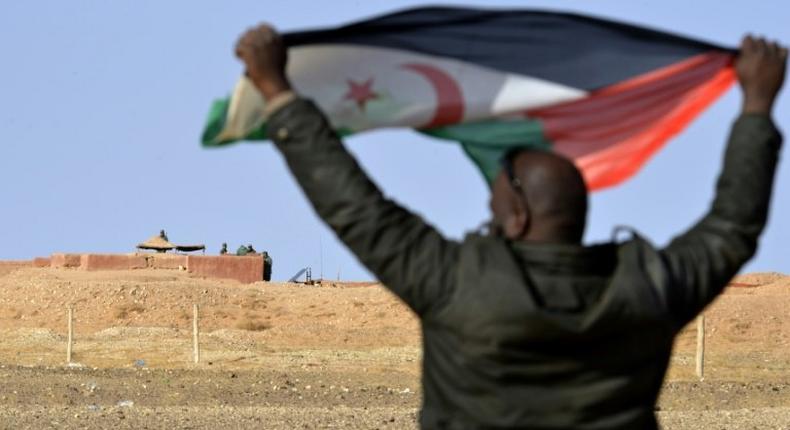 A Sahrawi man holds up a Polisario Front flag near Moroccan soldiers guarding the security barrier in contested Western Sahara