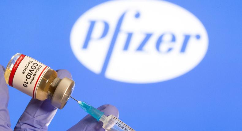 A coronavirus vaccine vial in front of the Pfizer logo.
