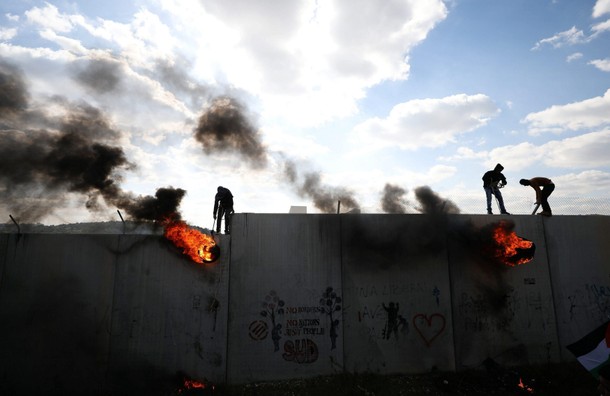 Palestinian protesters lift burning tyres as they climb over a section of the Israeli barrier during