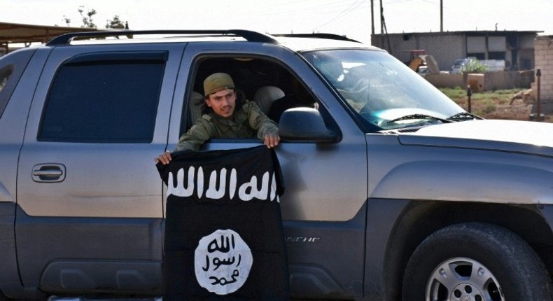 A member of the Syrian pro-government forces holds an Islamic State (IS) group flag after they entered the village of Dibsiafnan on the western outskirts of the Islamist's Syrian bastion of Raqa on June 11, 2017