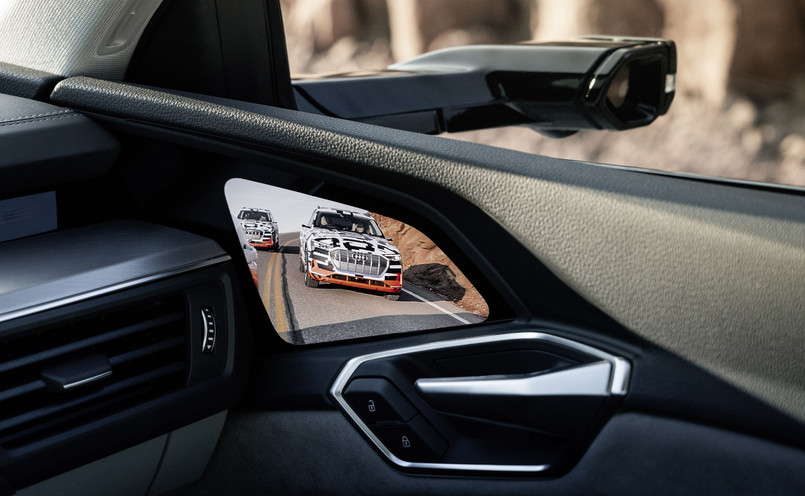 W Audi e-tron debiutują – w skali światowej jeśli chodzi o samochody produkowane seryjnie – opcjonalne, wirtualne lusterka zewnętrzne. To małe kamerki na płaskich wspornikach. Rejestrowany przez nie obraz wyświetlany jest na ekranach OLED umiejscowionych w przejściu między deską rozdzielczą, a drzwiami