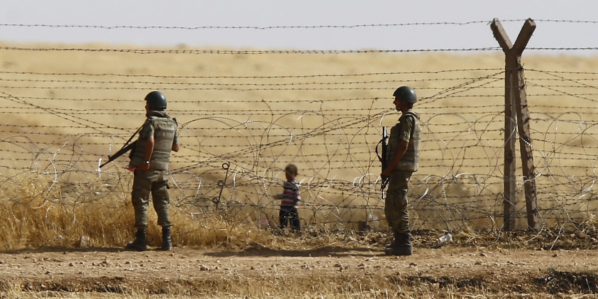 Turkish soldiers stand guard as a Syrian refugee boy waits behind the border fences to cross into Turkey on the Turkish-Syrian border, near the southeastern town of Akcakale in Sanliurfa province, Turkey, June 5, 2015.