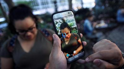 A Pokemon appears on the screen next to a woman as a man plays the augmented reality mobile game Pokemon Go by Nintendo in Bryant Park in New York City