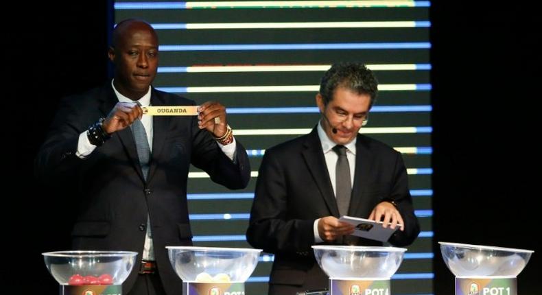 Fomer Senegalese football player Khalilou Fadiga (L) shows a piece of paper bearing the name of Ouganda next to Confederation of African Football (CAF) secretary general Hicham El Amrani during the 2017 African Cup of Nations draw ceremony