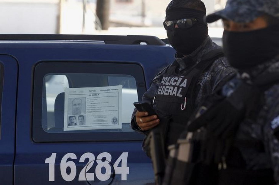 Mexican federal-police officers stand guard near a vehicle with a "Wanted" sign for then fugitive kingpin Joaquin "El Chapo" Guzman glued to the window, in Tijuana, October 24, 2015.