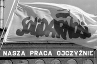 Flaga Solidarności, w tle napis propagandowy: Nasza praca ojczyźnie