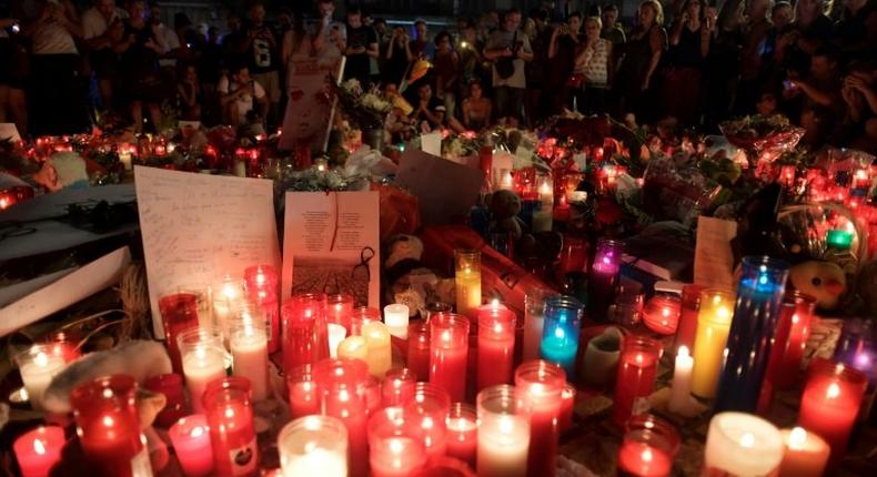 People stand next to flowers, candles and other items set up on the Las Ramblas boulevard in Barcelona