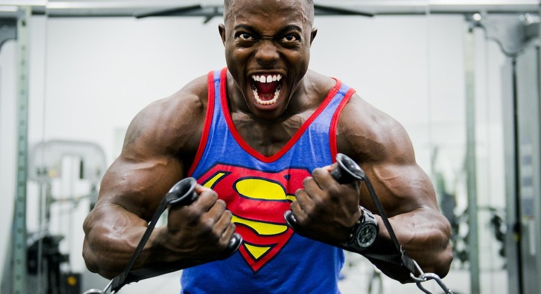 Man working out in the gym in a blue & red Superman print tank top shirt [Photo: Pixabay]