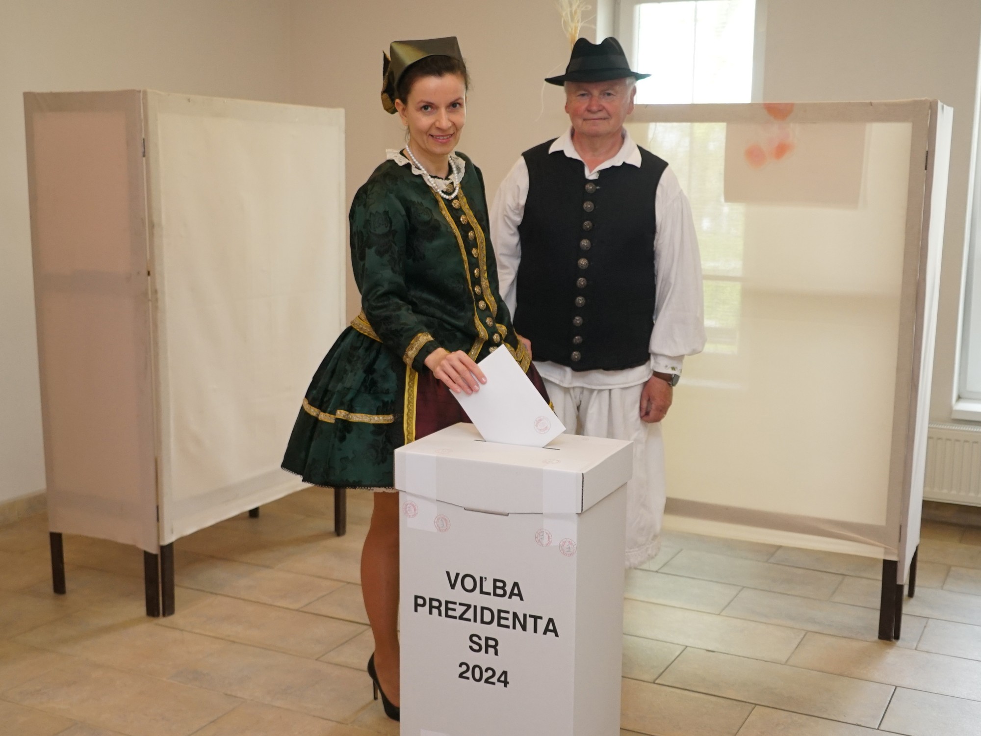 Členovia súboru ľudových tradícií Gyöngyösbokréta, ktorí prišli voliť v kroji, stoja pri členoch volebnej komisie vo volebnej miestnosti v 2. kole prezidentských volieb v obci Iža v okrese Komárno.
