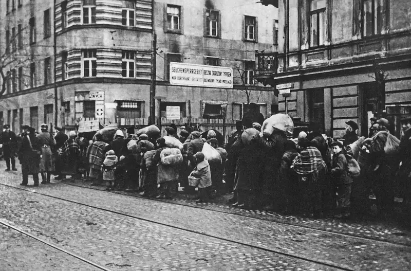 Przymusowe przesiedlenie ludności żydowskiej z mniejszych miast i osiedli w dystrykcie warszawskim do getta warszawskiego. Zdjęcie wykonano przy skrzyżowaniu ul. Żelaznej z al. „Solidarności” (d. ul. Leszno) / Domena publiczna Wikimedia Commons