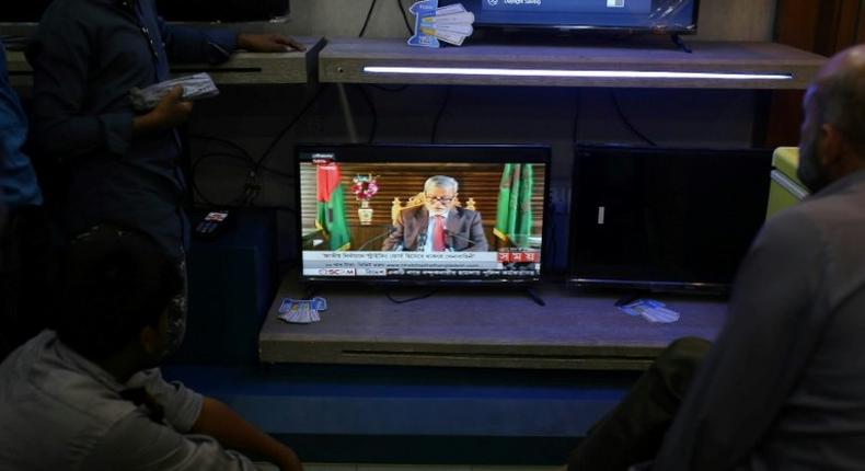 People watch television in an electric goods store in Dhaka as Chief Election Commissioner Nurul Huda addresses the nation on November 8, 2018