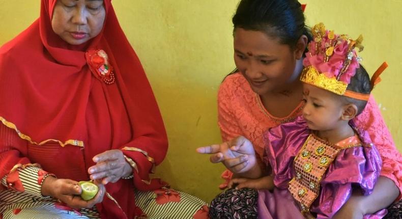 Toddler Salsa Djafar sits on her mother's lap during a circumcision ceremony in Gorontalo, Indonesia, led by a traditional healer