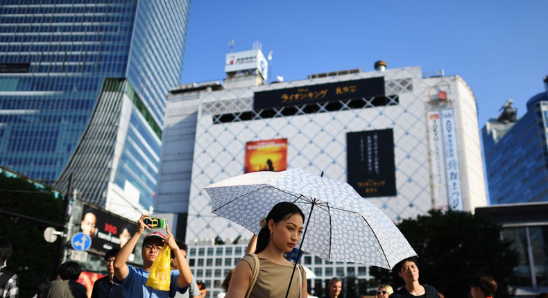 A woman protects herself from the sun with an umbrella during a heatwave as she crosses the street in Tokyo's Shibuya district on August 4, 2019.