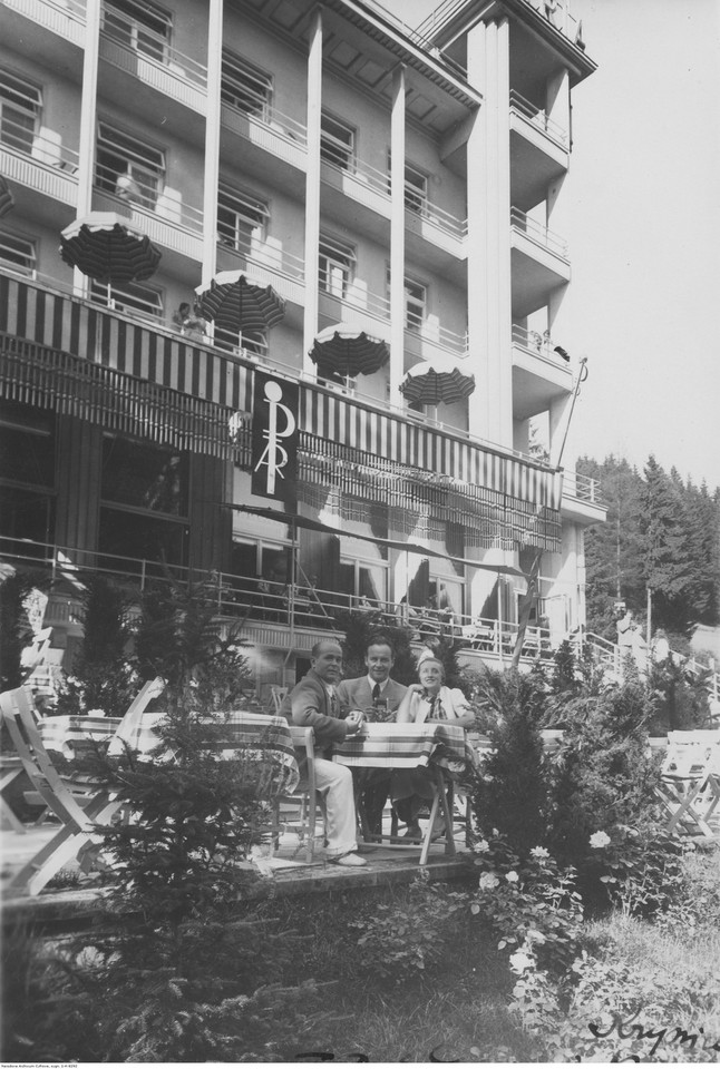 Śpiewak Władysław Kiepura (Ladis), aktor Igo Sym oraz piosenkarka, tancerka i aktorka Hanka Ordonówna siedzą przy stoliku przed hotelem Patria