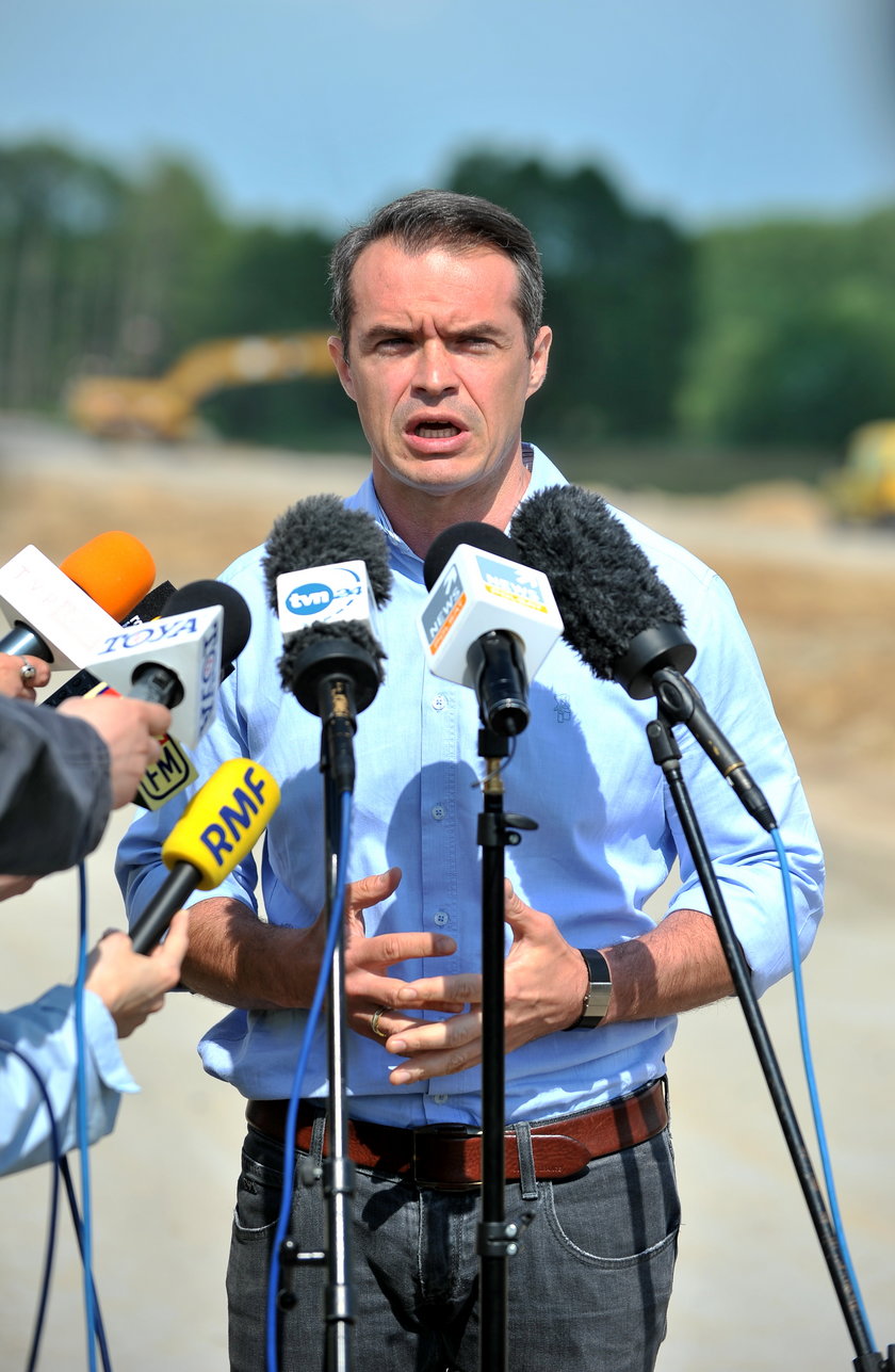 Minister Sławomir Nowak w niebieskiej koszuli z mikrofonami podcxzas konferencji na budowie S8