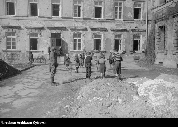 Grupa dzieci z opiekunką przed budynkiem Domu Dziecka (od 1946 r. im. Nieznanego Żołnierza) przy Rynku Nowego Miasta 4, 1945 r.
