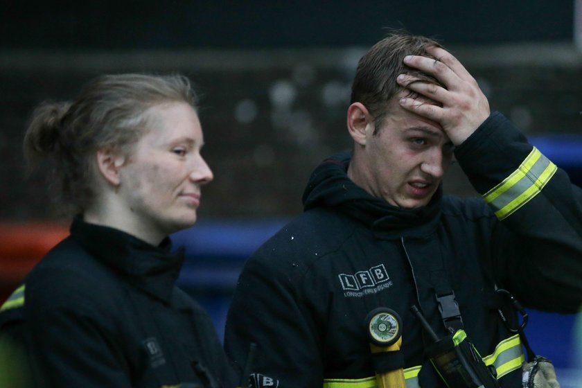 A police officer holds a riot shield over a firefighter at a tower block severely damaged by a serio