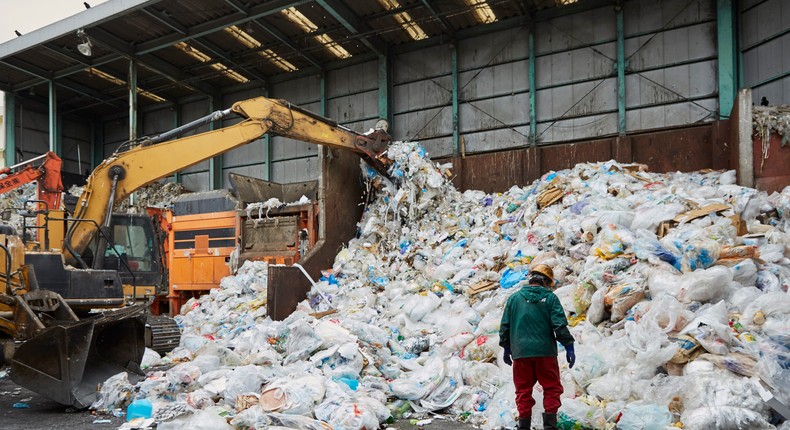 A worker stands in front of a pile of plastic waste as machinery processes it at a facility in Japan.