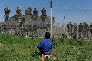 A boy sits on his ball next to a border fence on the Greek side of the border, as Macedonian police 