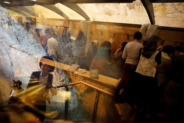 Ultra-Orthodox Jewish youth are reflected in a glass panel as female Jewish worshippers pray next to