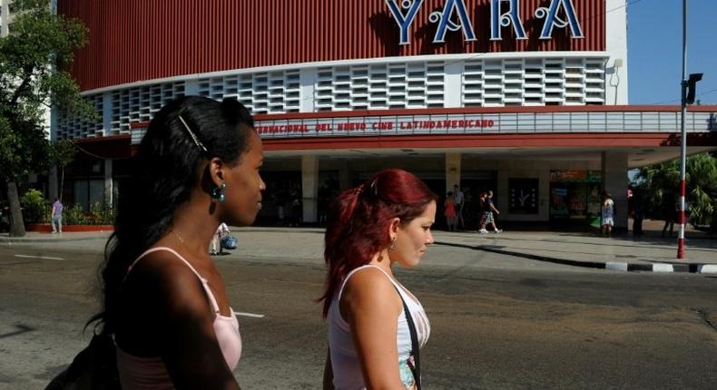 Cubans walk past a movie theater announcing the Havana Latin American Film Festival