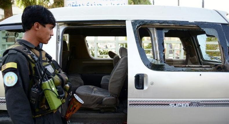 An Afghan policeman inspects a damaged vehicle in Kandahar on December 17, 2016, in which five female airport workers were killed