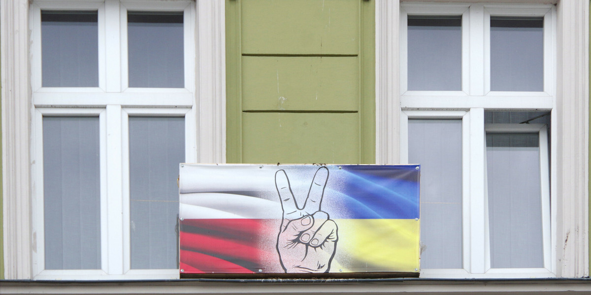 Bilboard rozwieszony miedzy oknami kamienicy przedstawiający połączone flagi Polski i Ukrainy ze znakiem "V" symbolem zwycięstwa i wolności.